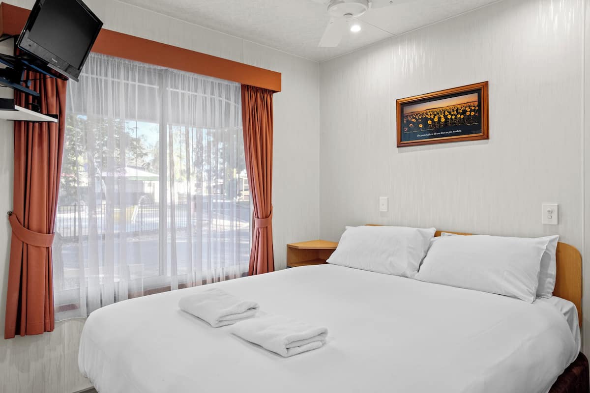 A neatly made bed with white linens, a television mounted on the wall, and a framed picture above the bed.