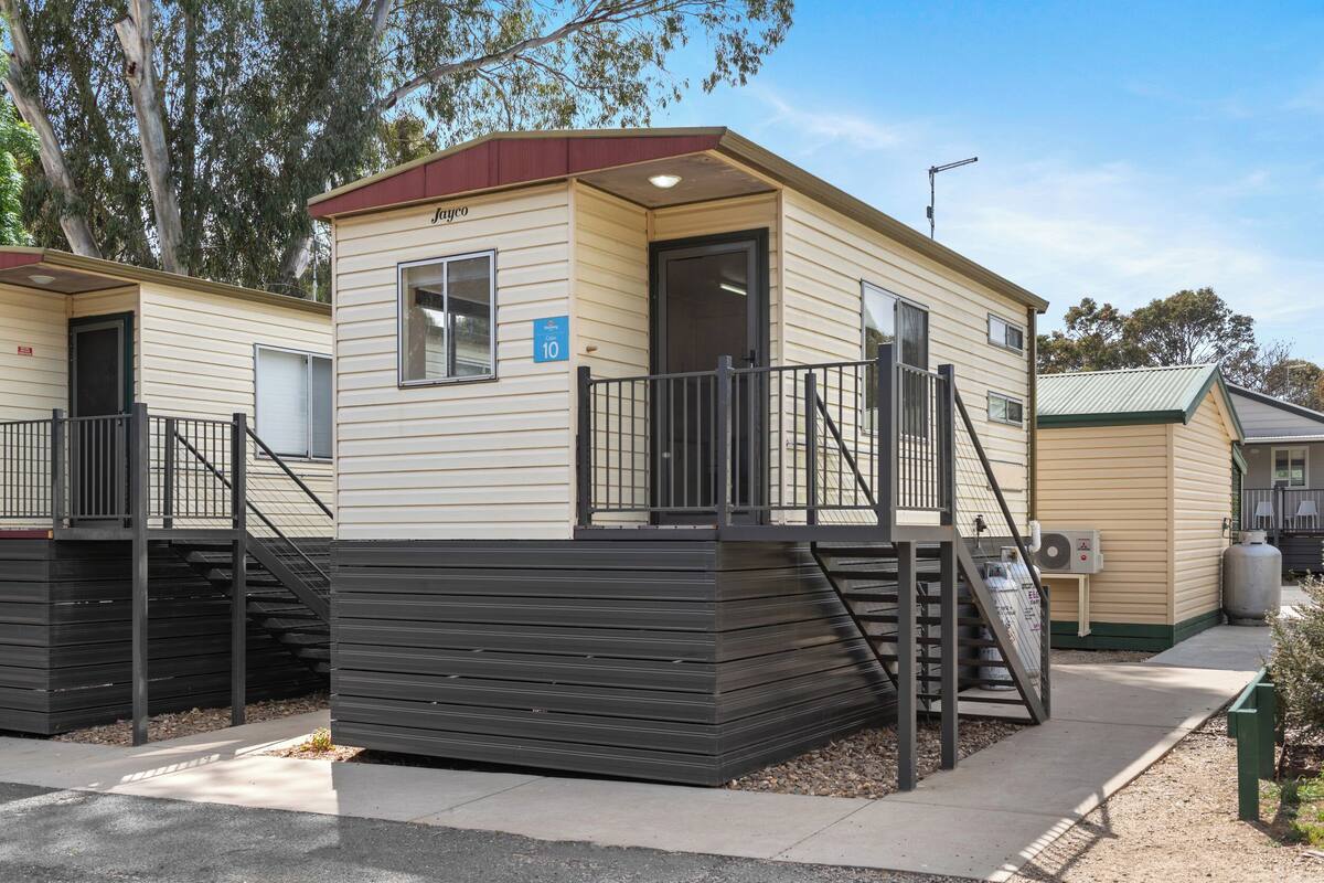A single-story mobile home with a beige exterior, a dark brown roof, and a small porch with a black railing.