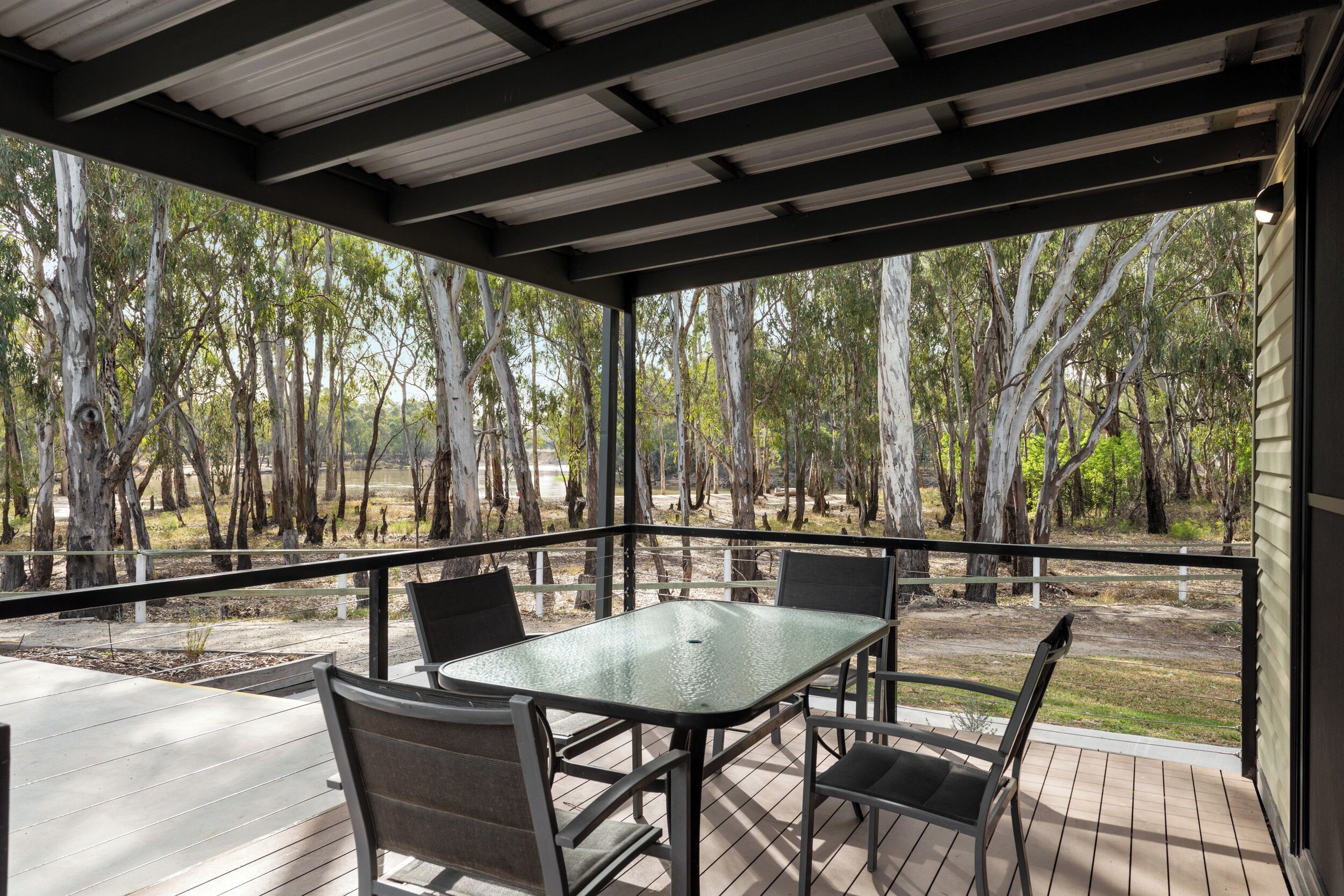 Une terrasse extérieure couverte, avec une table et des chaises, entourée d’arbres.