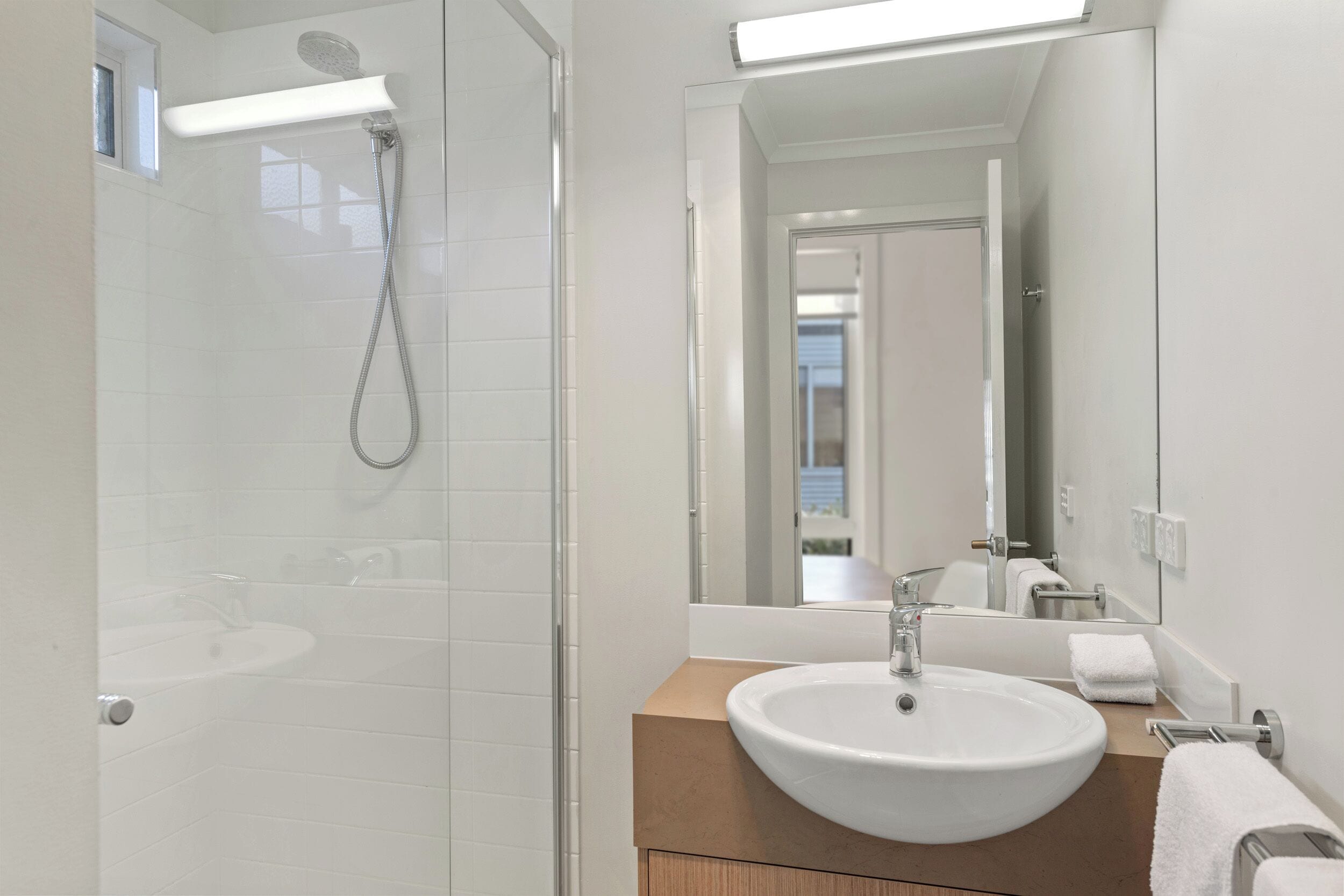 A modern bathroom with a glass-enclosed shower, a white sink, and a large mirror.