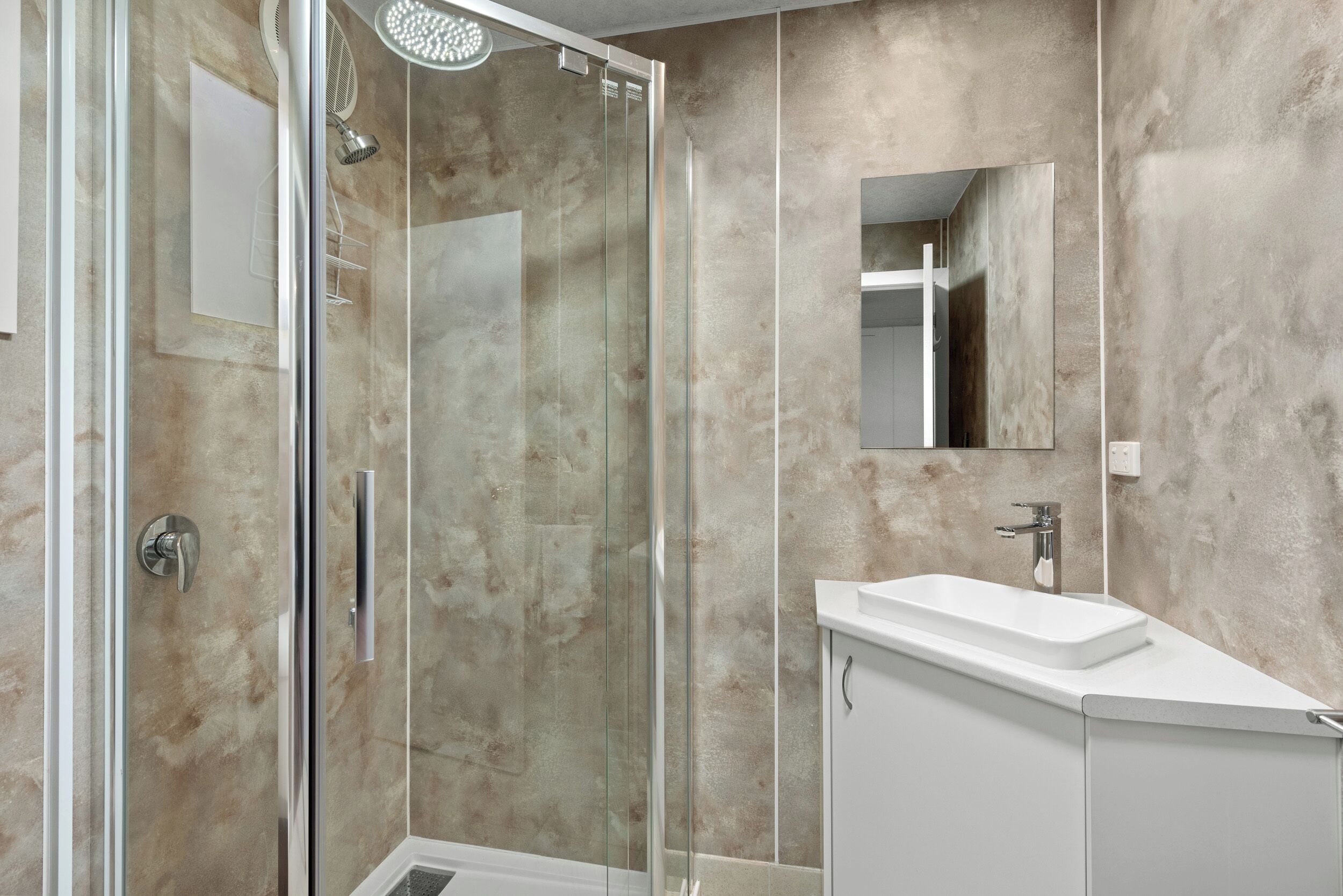 Un baño moderno con cabina de ducha de vidrio, lavamanos blanco y un espejo grande.