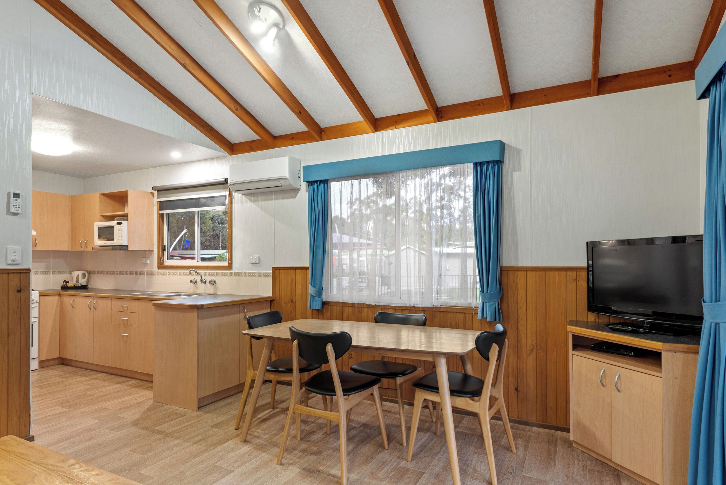 A compact kitchen with wooden cabinets, a microwave, and a dining area with a table and chairs.