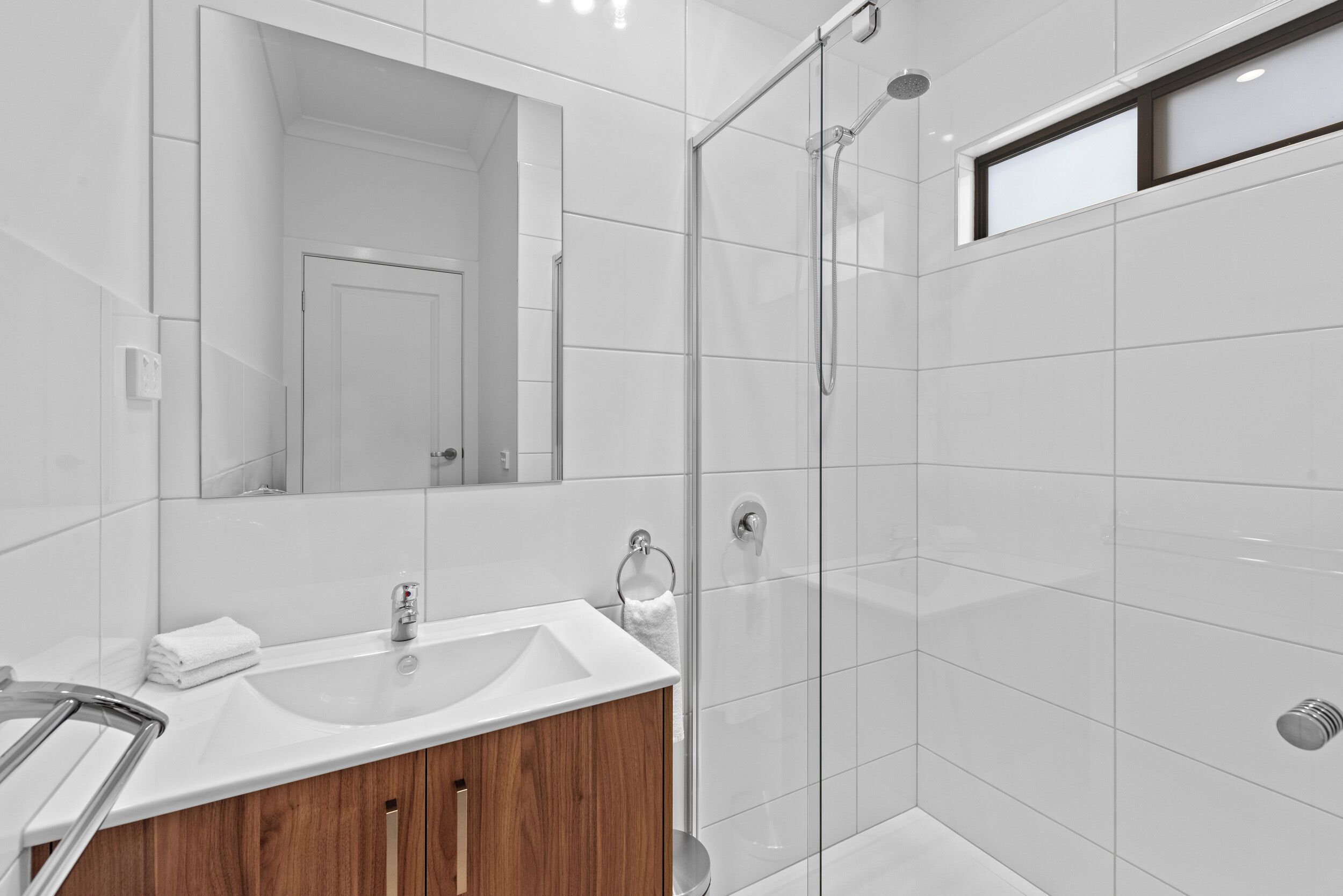A modern bathroom with a glass shower enclosure, a sink with a wooden vanity, and a large mirror.