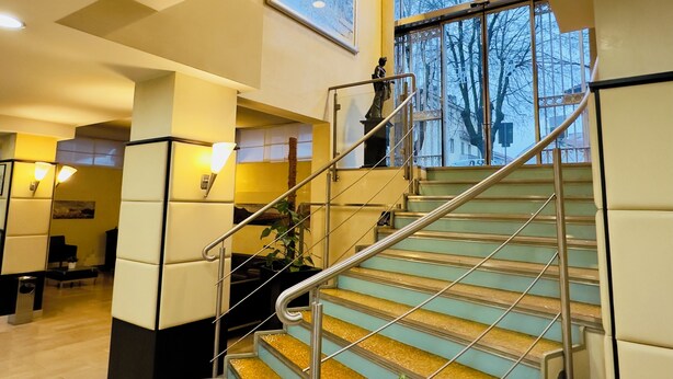 Un moderno vestíbulo de hotel con una escalera, una estatua y un gran ventanal con vistas a árboles.