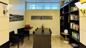 Una habitación pequeña con una mesa de comedor, sillas, una estantería y dos ventanas amplias.