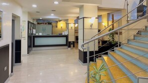 Un vestíbulo de hotel con un mostrador de recepción, una escalera y un cuadro en la pared.