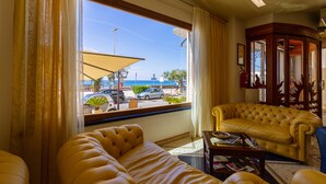 A room with a large window, a yellow sofa, a small table, and a wooden cabinet. - Hotel Riva del Sole (Cefalù)