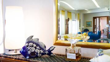 A room with a large mirror reflecting a yellow sofa and a wooden cabinet. A decorative fish sculpture and a bottle of Quiletteson are on a table.