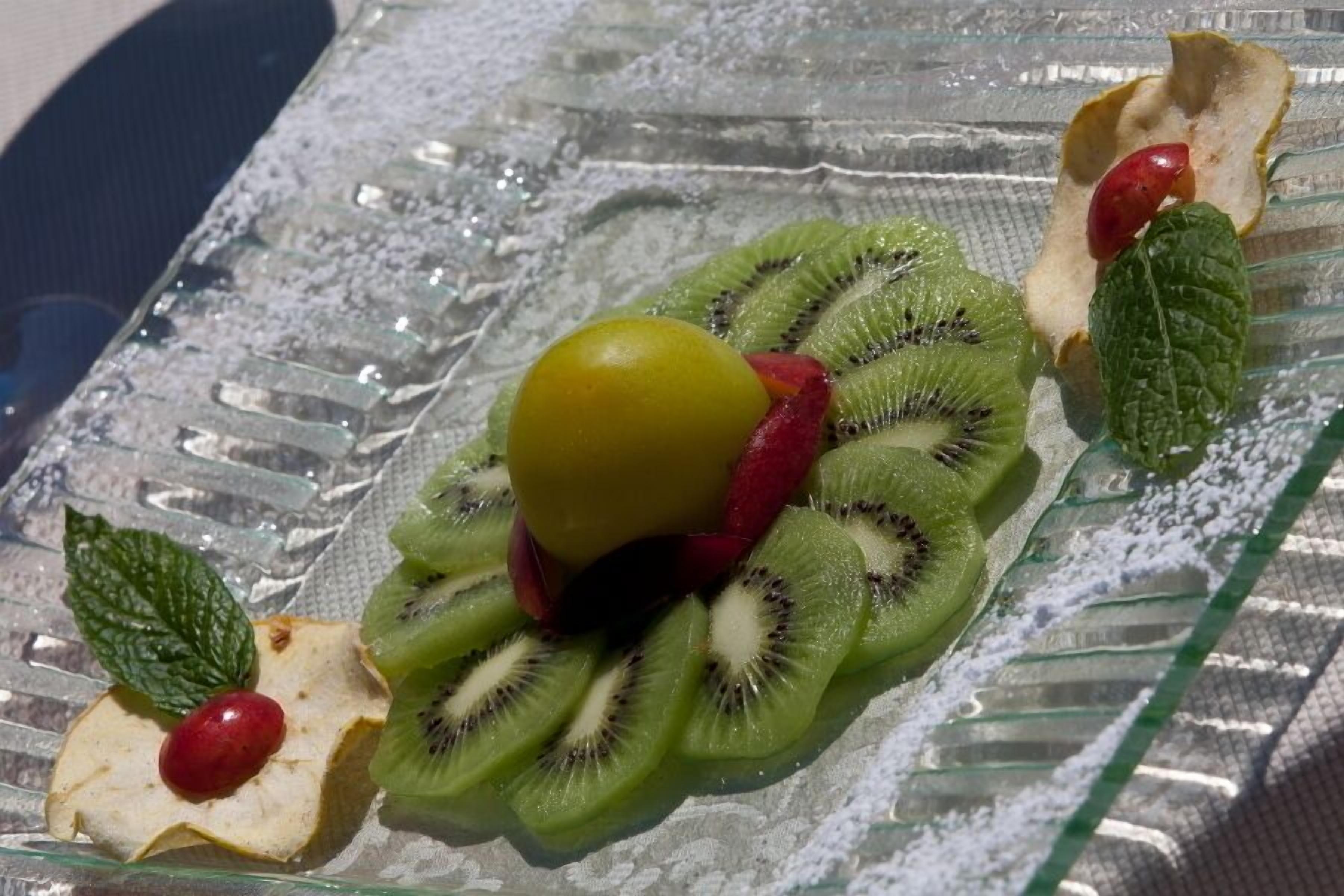 A dessert plate with sliced kiwi, a cherry, and a mint leaf.