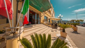 A hotel entrance with steps leading up to the door, outdoor seating, and potted plants. - Hotel Riva del Sole (Cefalù)