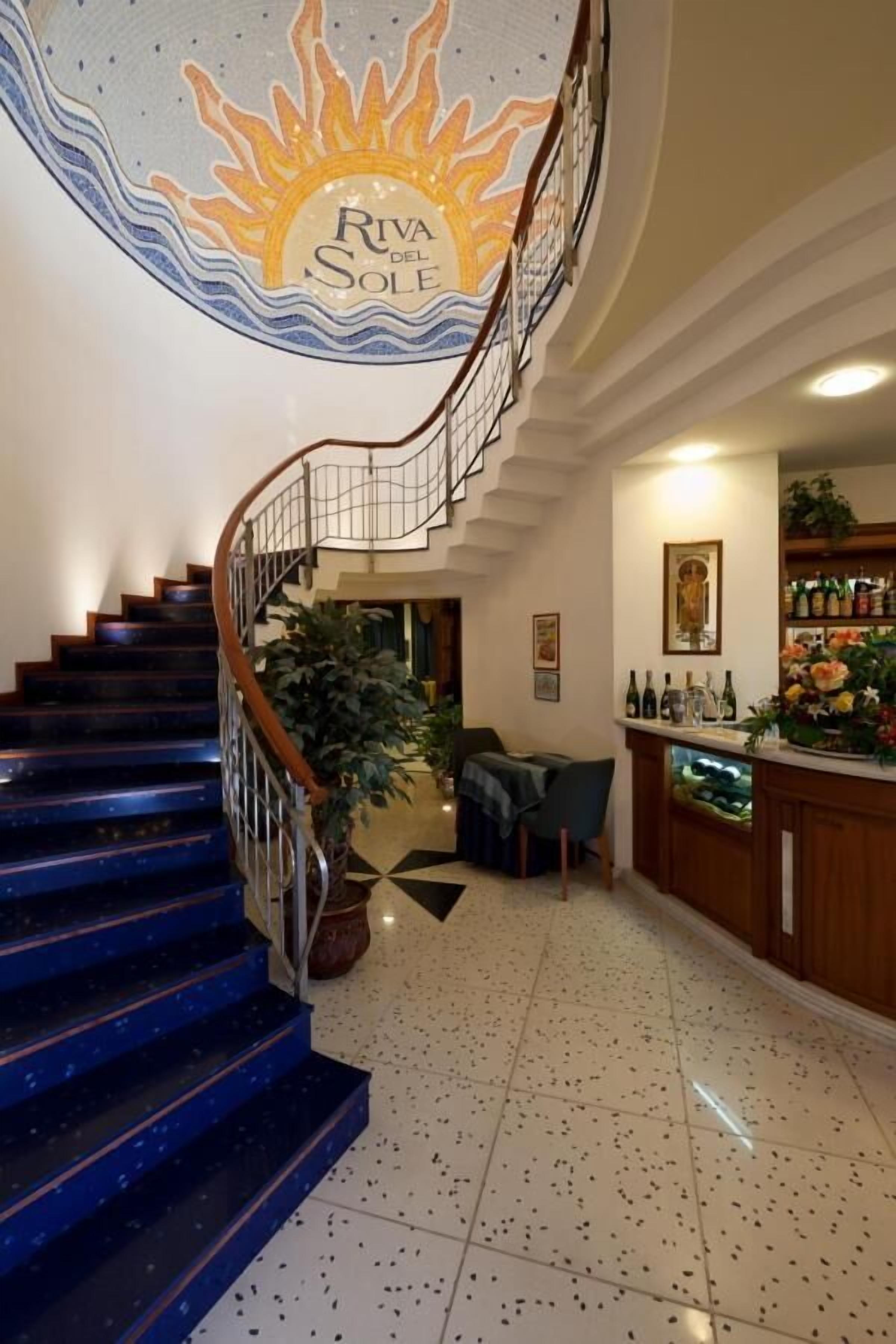A spiral staircase with a sun mural, a bar area with bottles, and a dining area with a table and chairs.
