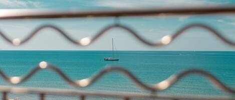 Vista de una playa con un velero a lo lejos, un flotador salvavidas y sombrillas en la cubierta.