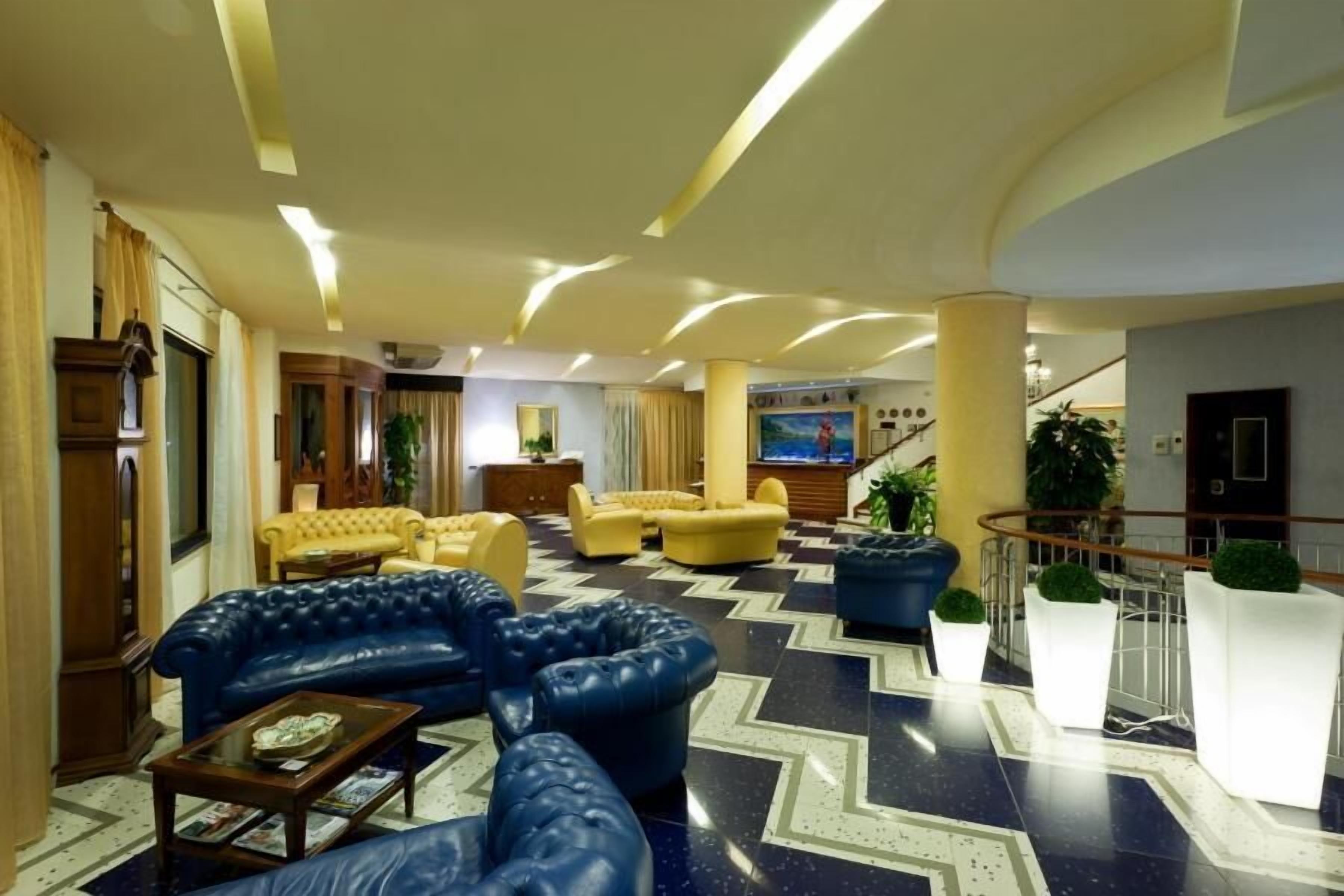 A spacious lobby with a blue leather sofa, yellow armchairs, and a large TV screen.