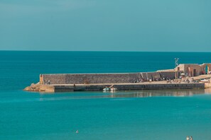 A coastal fortification with a clear view of the sea, a small boat docked near the structure, and a few people visible on the promenade.