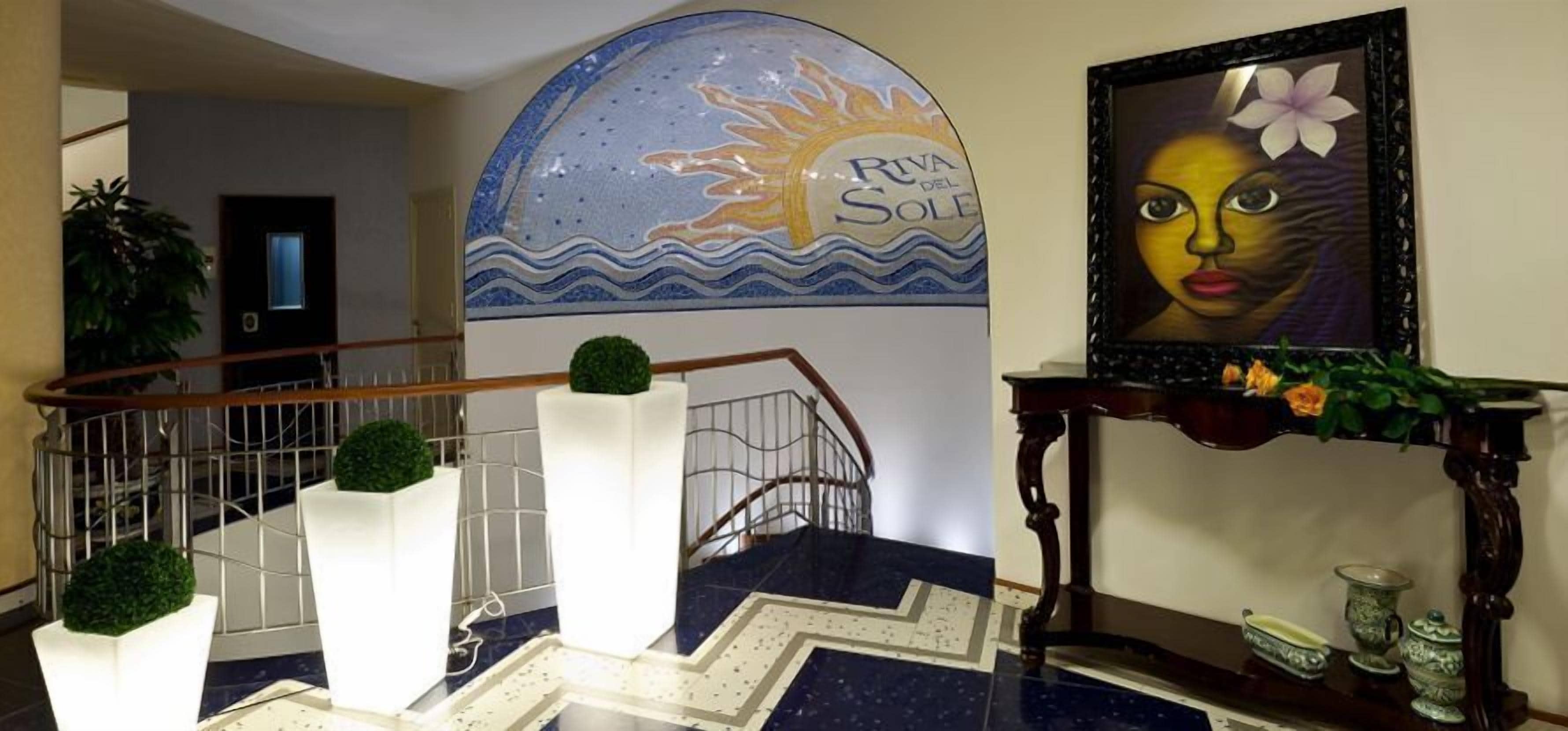 A staircase with a handrail, white pillars, and a decorative wall with a sun and waves design.