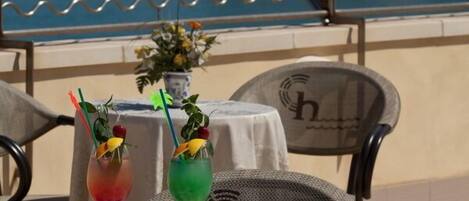 A table with drinks and a flag, overlooking a coastal area with buildings and the sea.