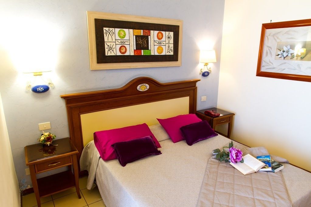 A neatly made bed with two bright pink pillows, a wooden headboard, a bedside table with a lamp, and a framed artwork above the bed.