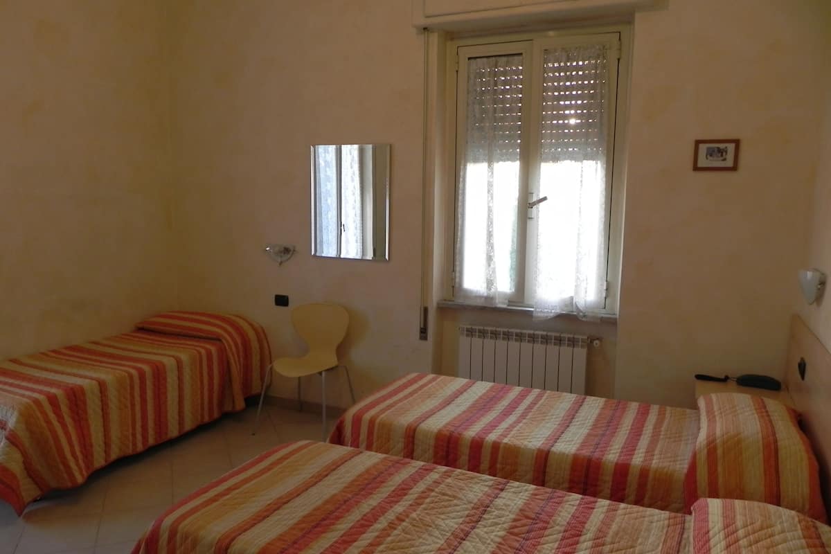 Une chambre avec deux lits simples, une chaise, un radiateur et une fenêtre avec des rideaux en dentelle.
