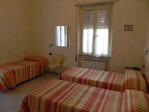 Ein Zimmer mit zwei Einzelbetten, einem Sessel, einem Heizkörper und einem Fenster mit Spitzenvorhängen.