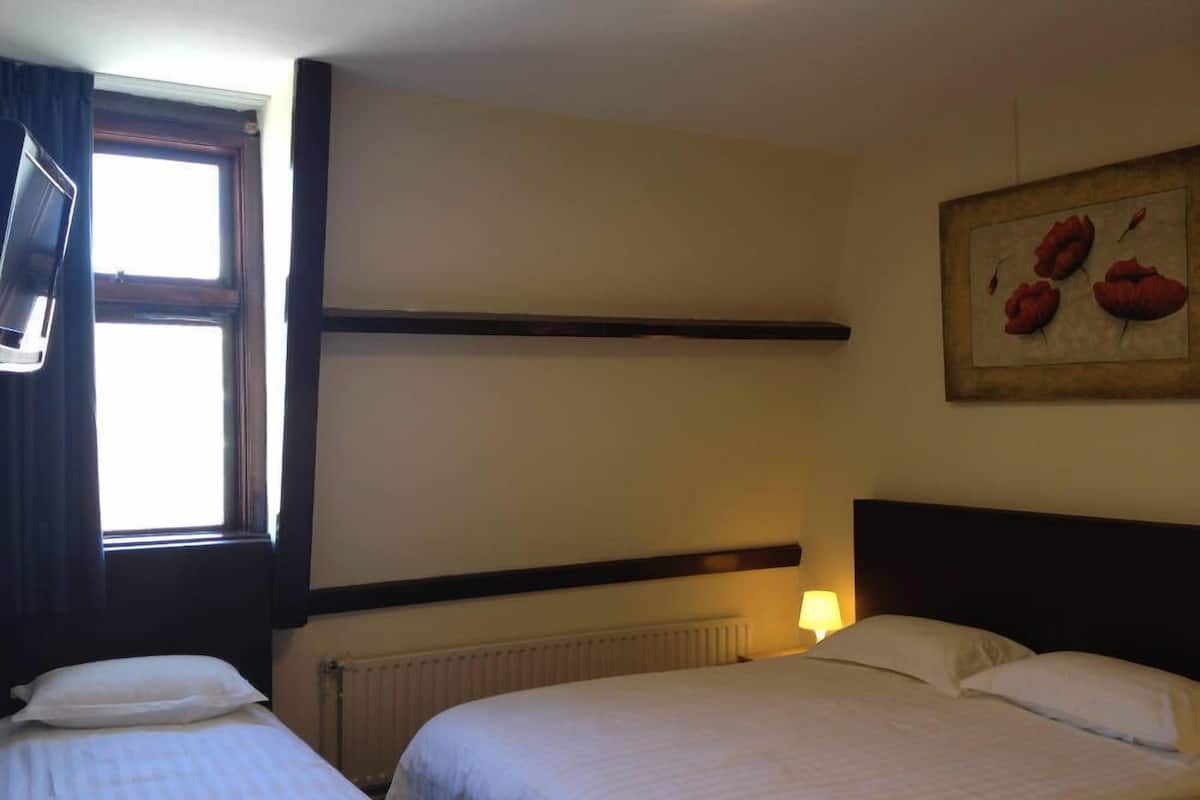 Une chambre d’hôtel avec deux lits, une fenêtre, un radiateur et un tableau au mur.
