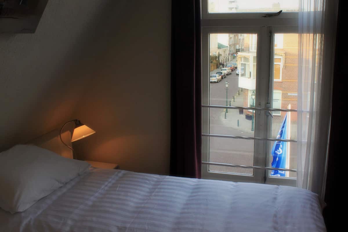 Une chambre d’hôtel avec un lit, une lampe et une vue sur la rue, visible par la fenêtre.