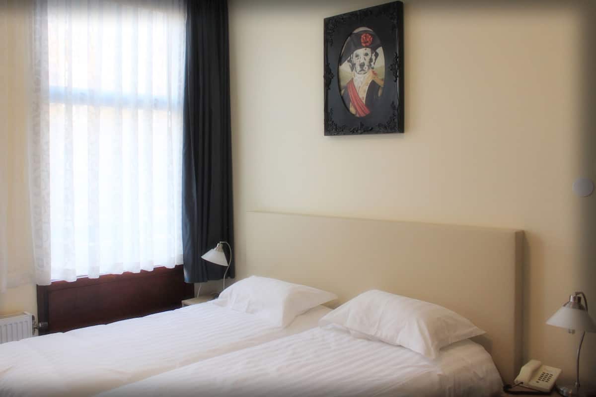 Une chambre d’hôtel avec un grand lit, une table de chevet avec une lampe, un tableau au mur et une fenêtre avec des rideaux.