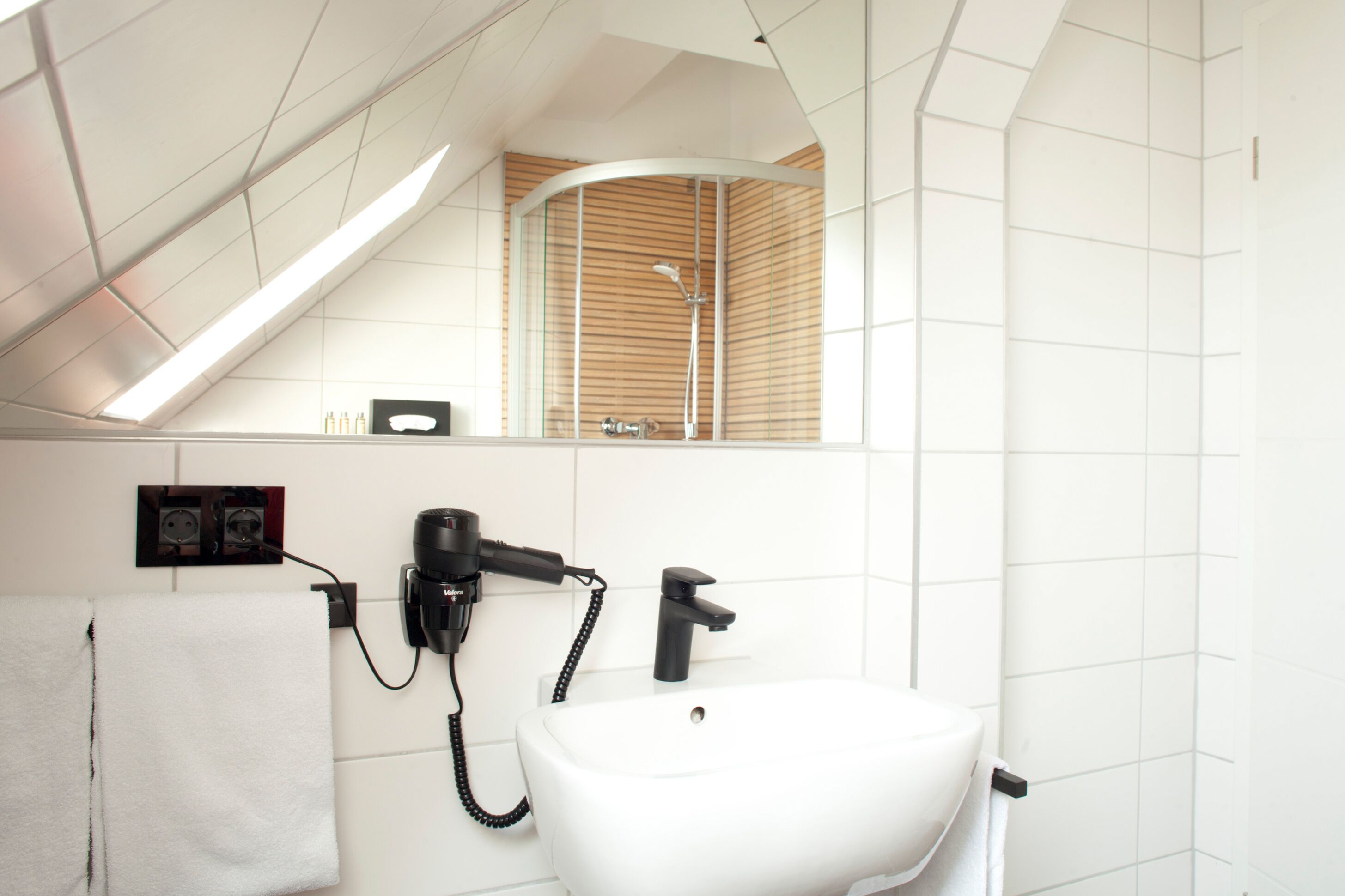 Een moderne badkamer met dakraam, een witte wastafel en een haardroger.