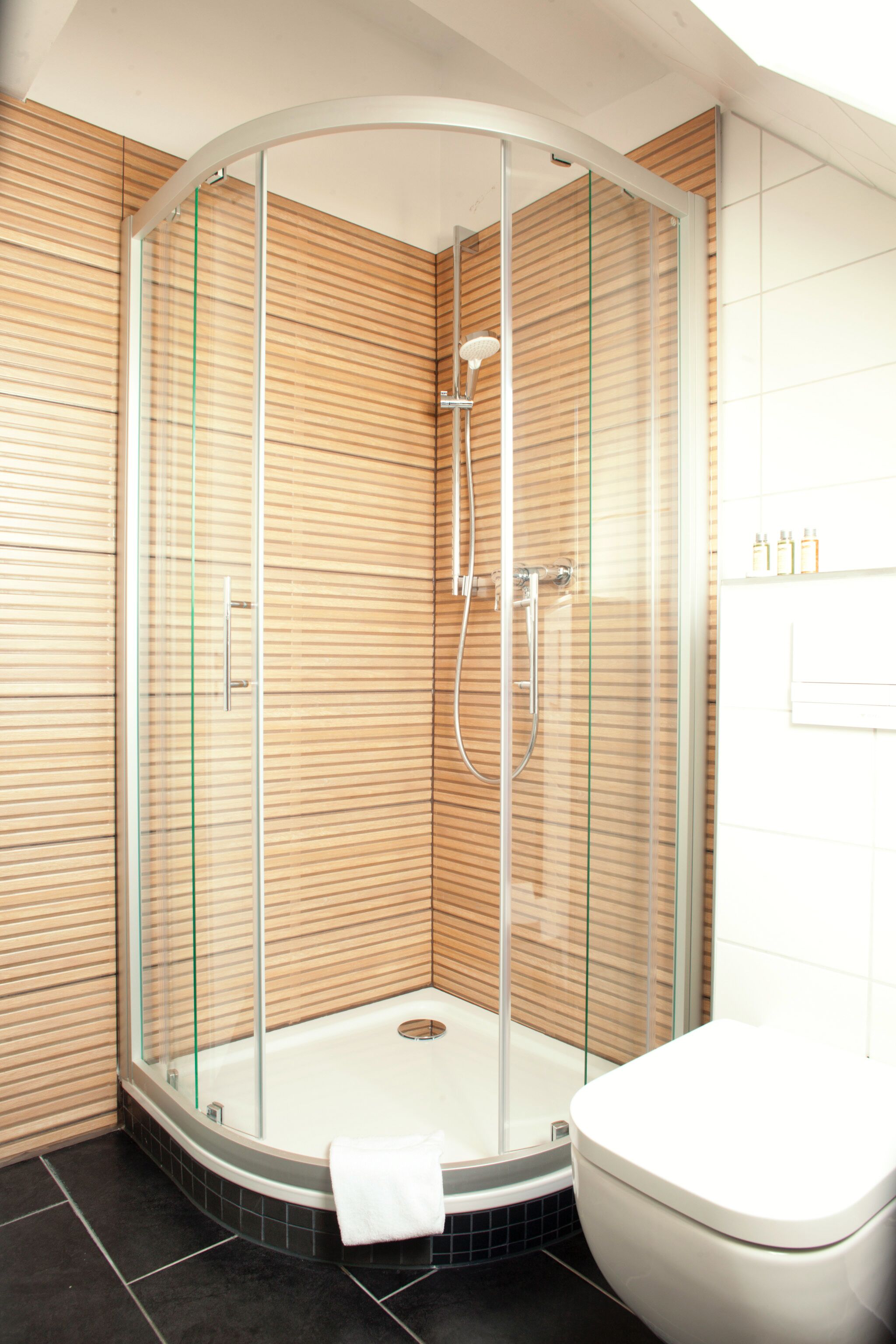 Un bagno moderno con doccia vetro, WC bianco e pannelli in legno sulle pareti.