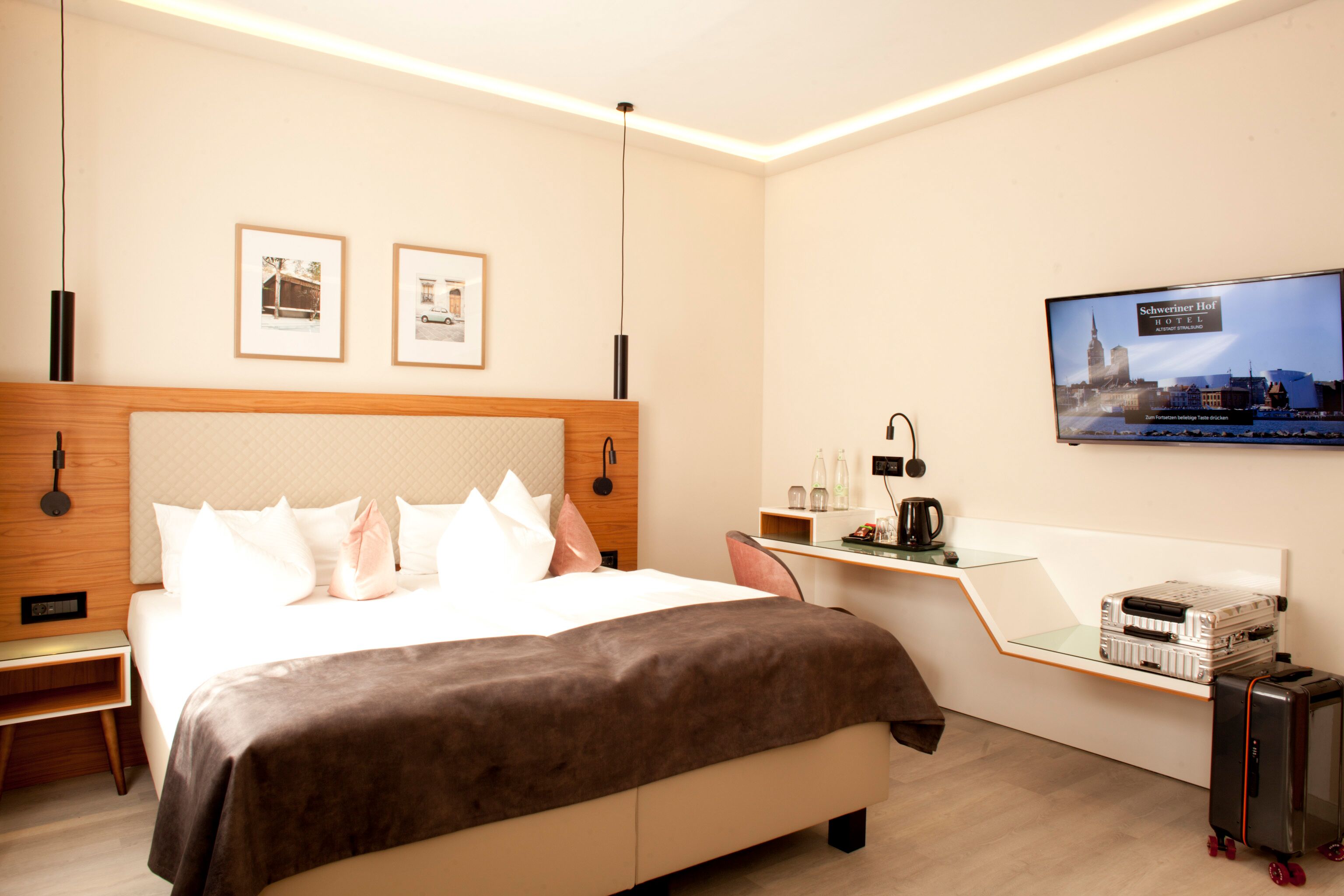 A modern hotel room with a large bed, a desk, a television, and a minibar.