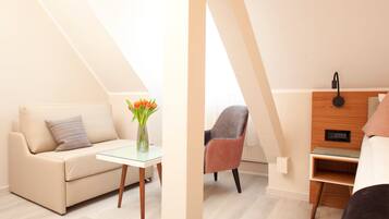 Una habitación moderna y luminosa con sofá, una mesita con un florero, una silla y una mesita de noche de madera con lámpara.