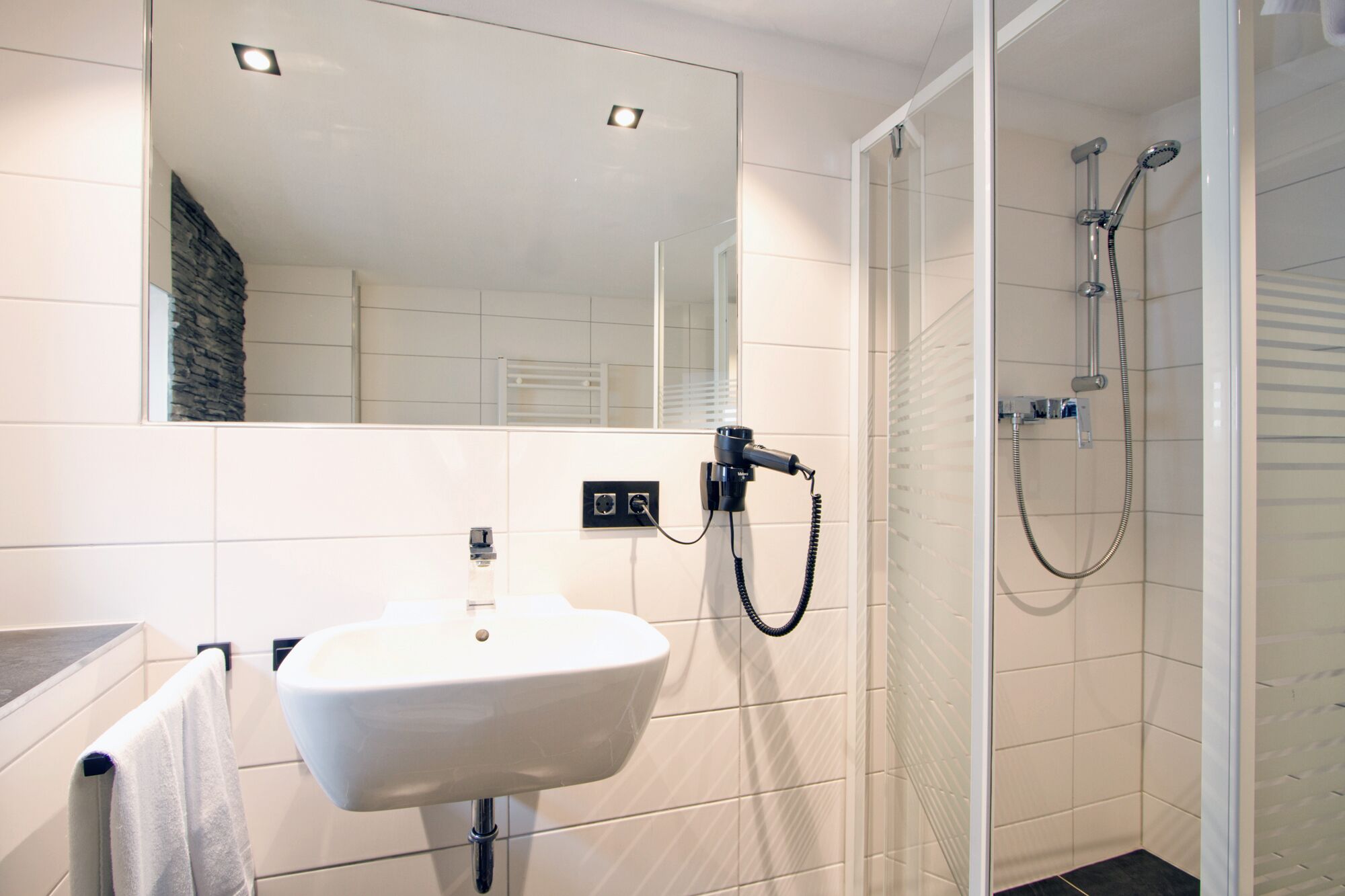 Une salle de bain avec un lavabo blanc, un miroir et une douche.