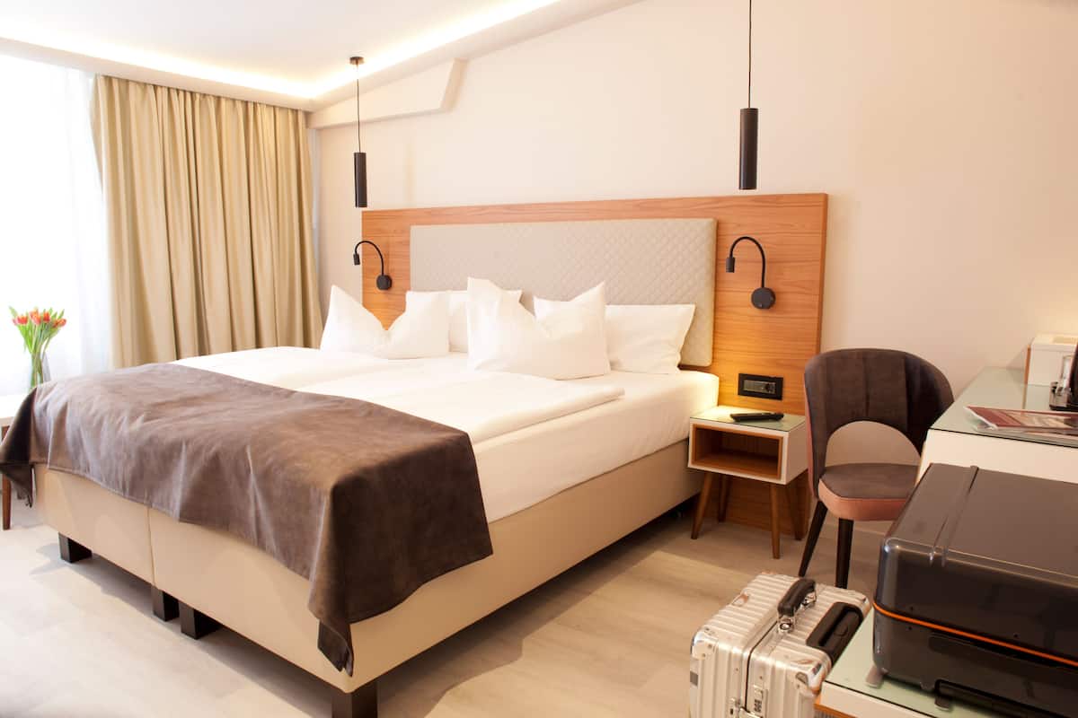 Habitación de hotel con una cama grande, mesitas de noche, un escritorio con silla y una maleta.