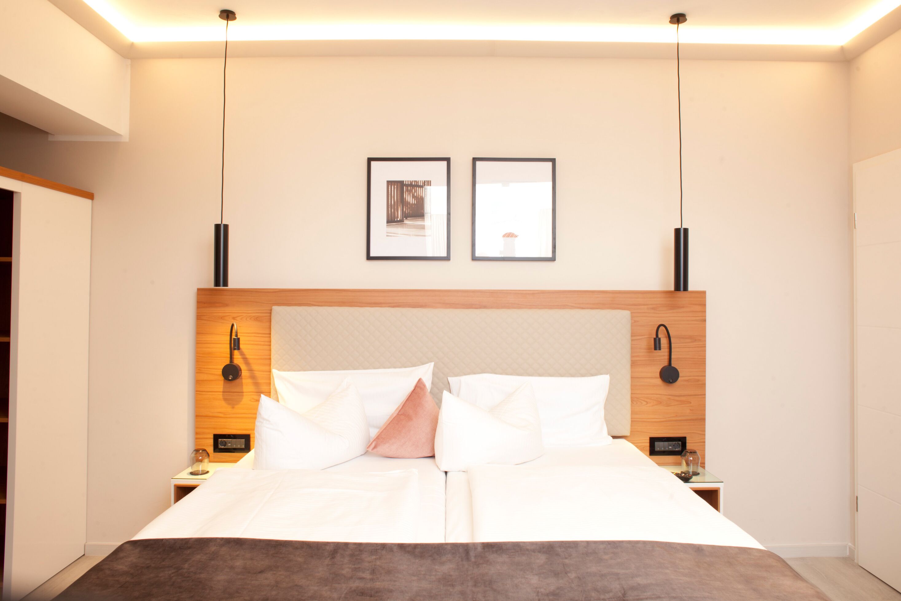 Una habitación de hotel moderna con una cama grande, dos mesitas de noche, un cabecero de madera y dos cuadros enmarcados en la pared.