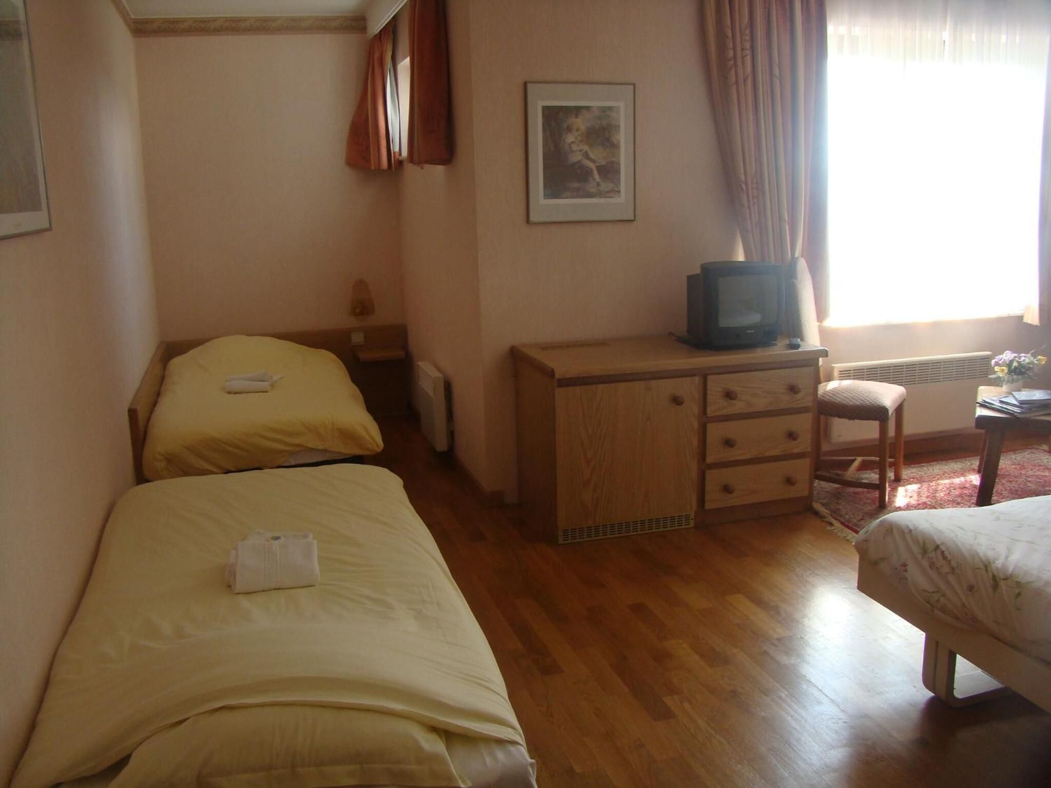 Una habitación con dos camas individuales, un escritorio de madera con televisor y un radiador.