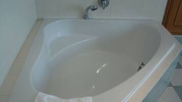 Uma banheira de imersão branca com uma única torneira, uma toalha sobre a borda e um chão ladrilhado.