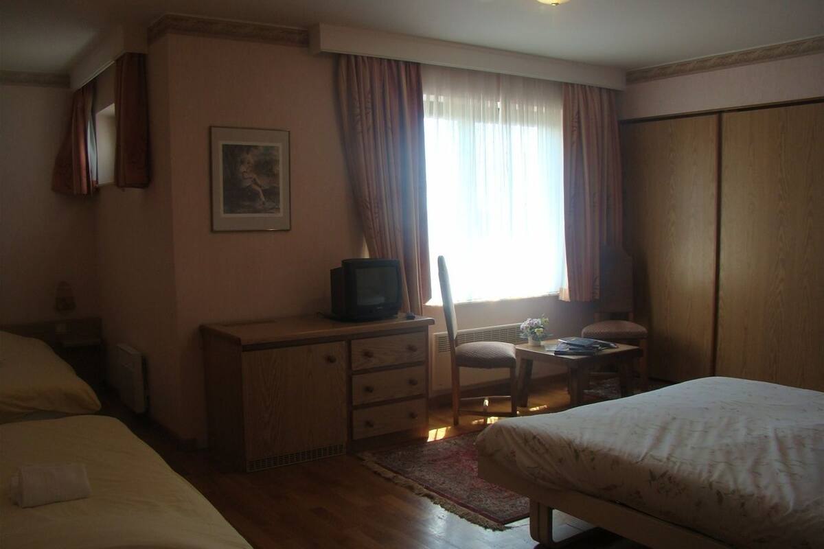 Une chambre d’hôtel avec deux lits, un bureau, une chaise, une télévision et une fenêtre avec des rideaux.
