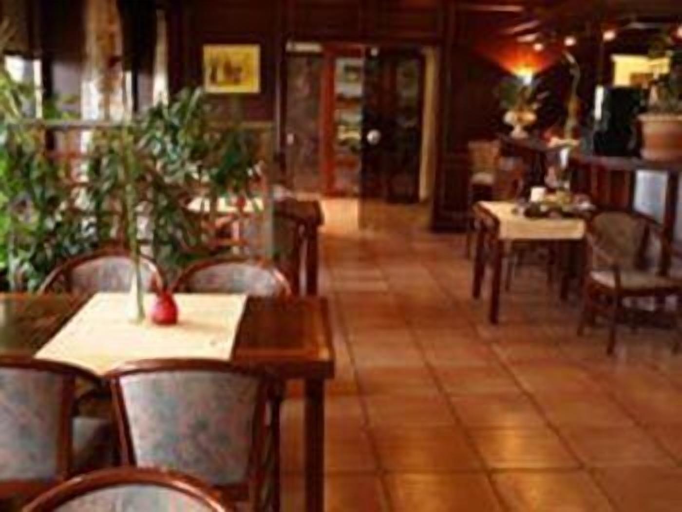 A restaurant interior with wooden tables and chairs, a tiled floor, and potted plants.