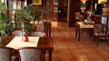 A restaurant interior with wooden tables and chairs, a tiled floor, and potted plants.