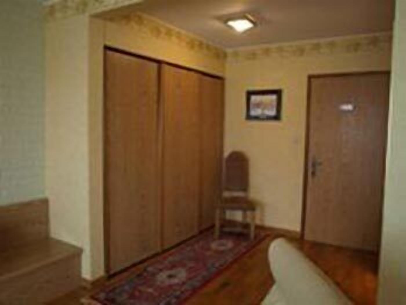 Um corredor com portas de madeira, uma cadeira e um tapete estampado.