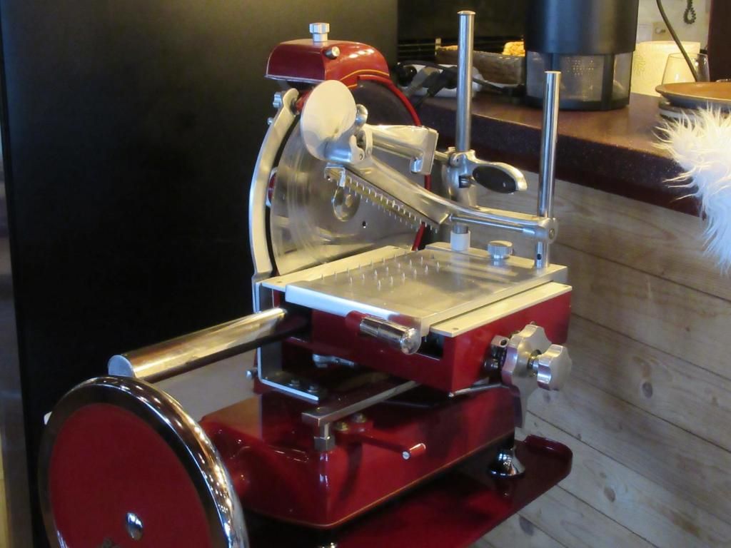 A red and silver meat slicer with a metal table and a handle.