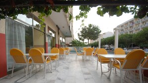 An outdoor patio with yellow chairs and white tables, surrounded by buildings and greenery. - Dias (Kusadasi)