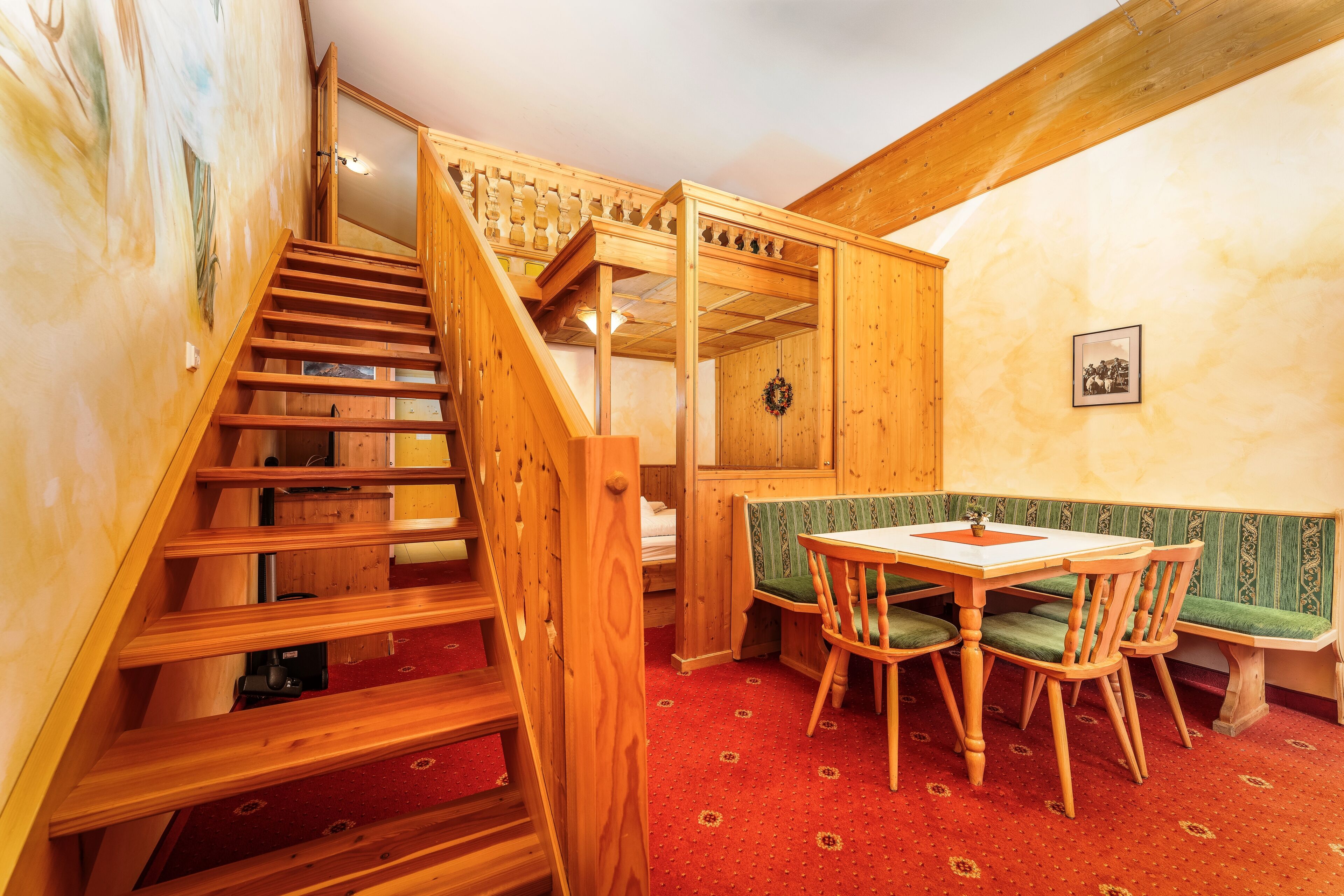 Una escalera de madera conduce a un dormitorio en buhardilla con literas, un comedor con mesa y sillas, y un banco.