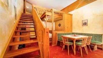 Una escalera de madera conduce a un dormitorio en buhardilla con literas, un comedor con mesa y sillas, y un banco.
