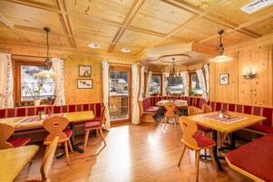 Ein Holzinneres mit Holzbänken und -tischen, einer Kristallleuchtre und gerahmten Bildern an den Wänden.