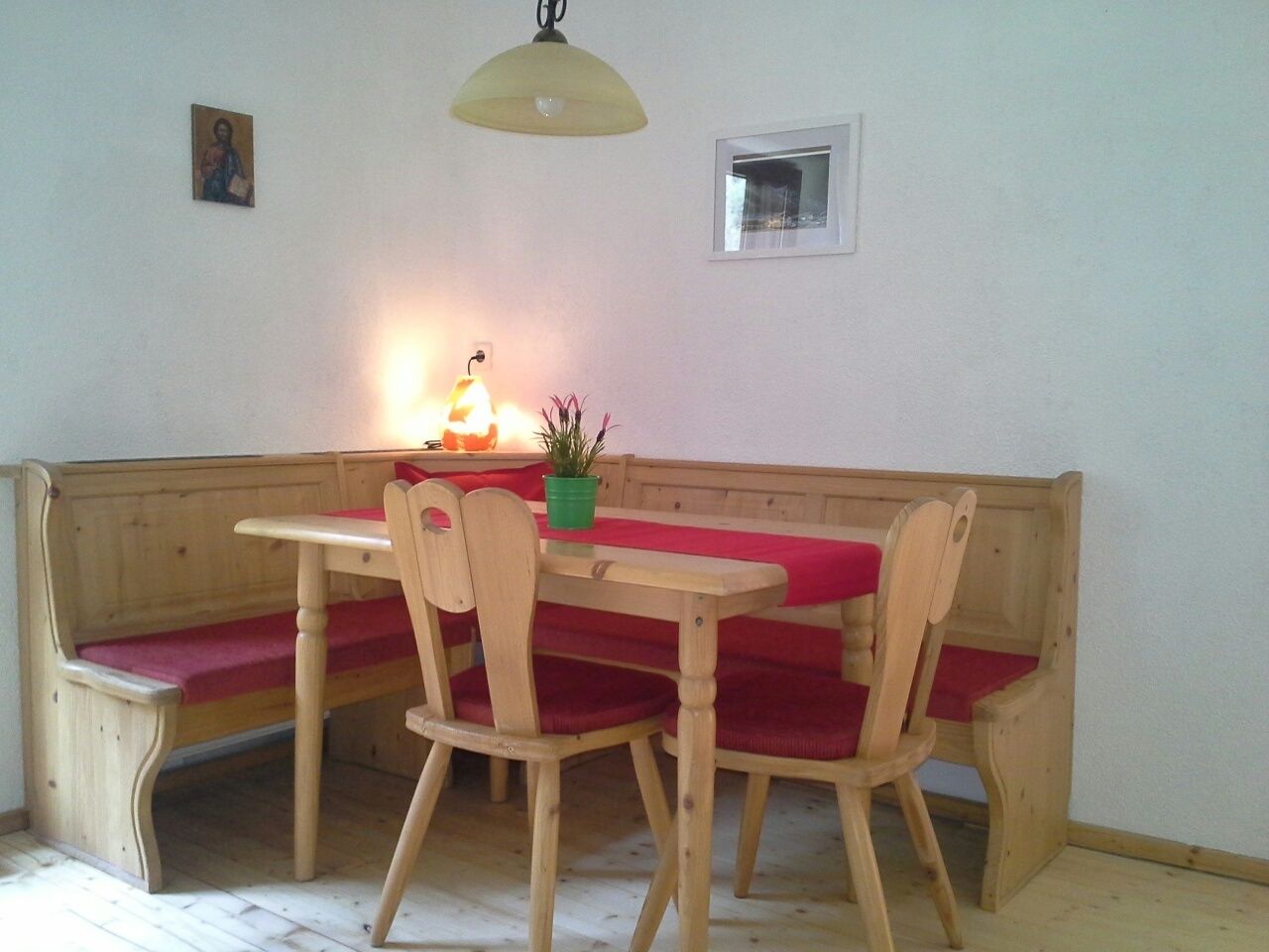 A wooden bench with red cushions, a table, and a hanging lamp.