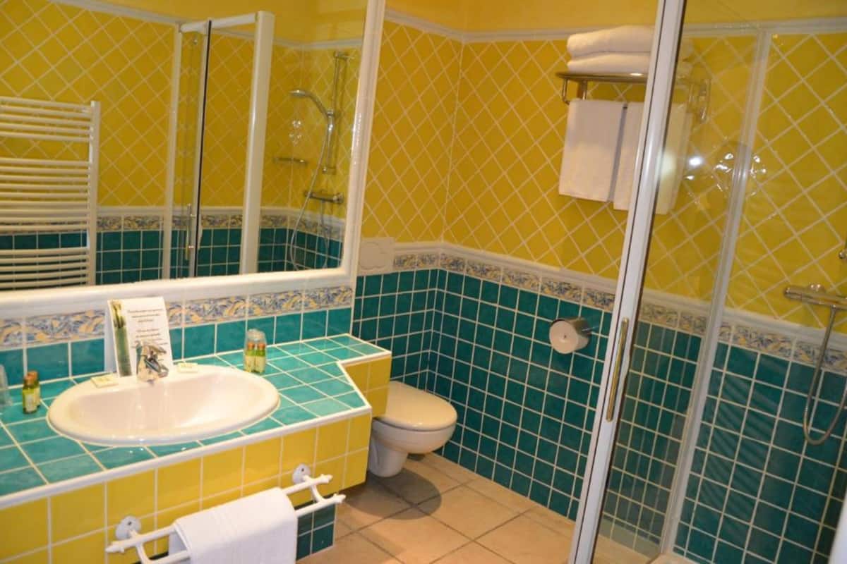 Un baño con pared de azulejos amarillos y azules, un lavamanos blanco y un inodoro.