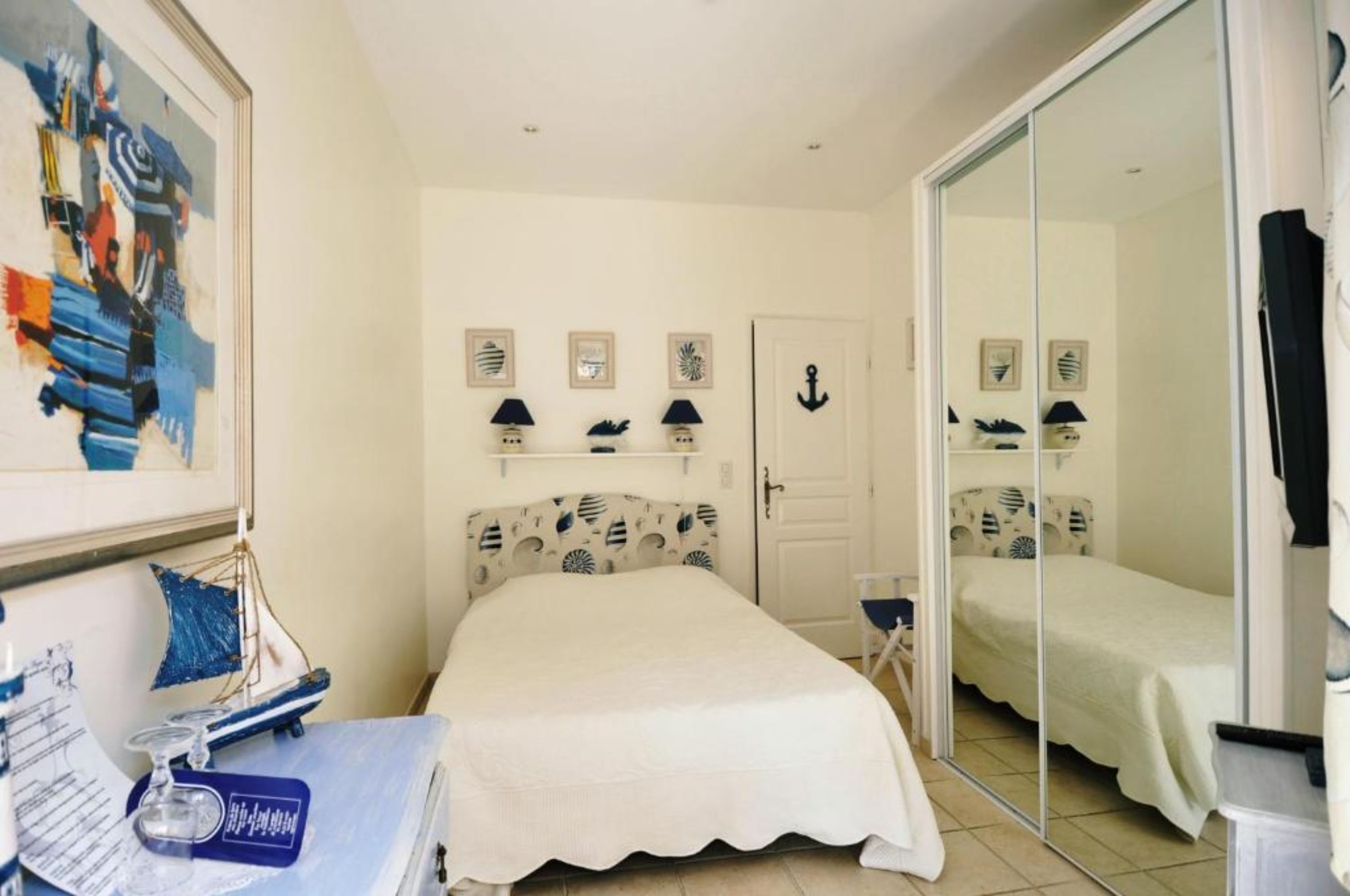A bedroom with a bed, a desk with a chair, a mirror, and a door.