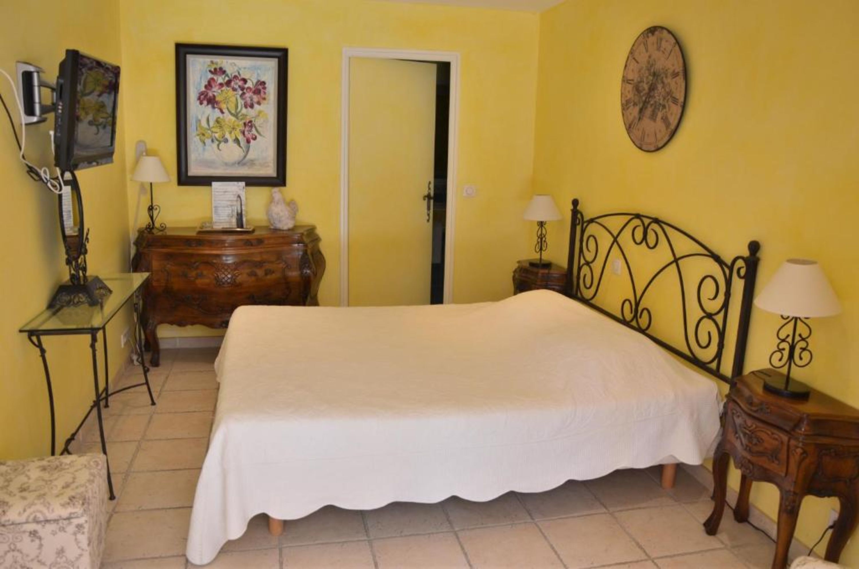 A bedroom with a bed, a dresser, a desk, a chair, a door, and a wall clock.