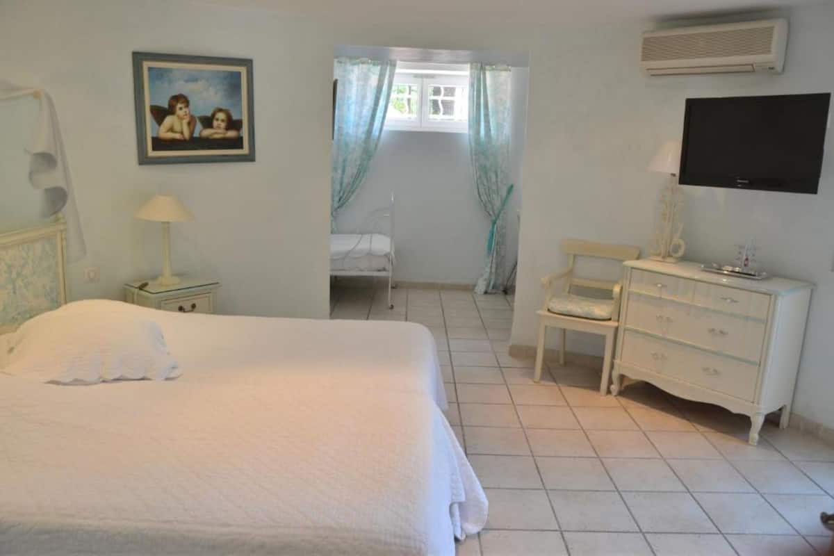 Un dormitorio con cama, mesita de noche, cómoda, televisor y ventana con cortinas.