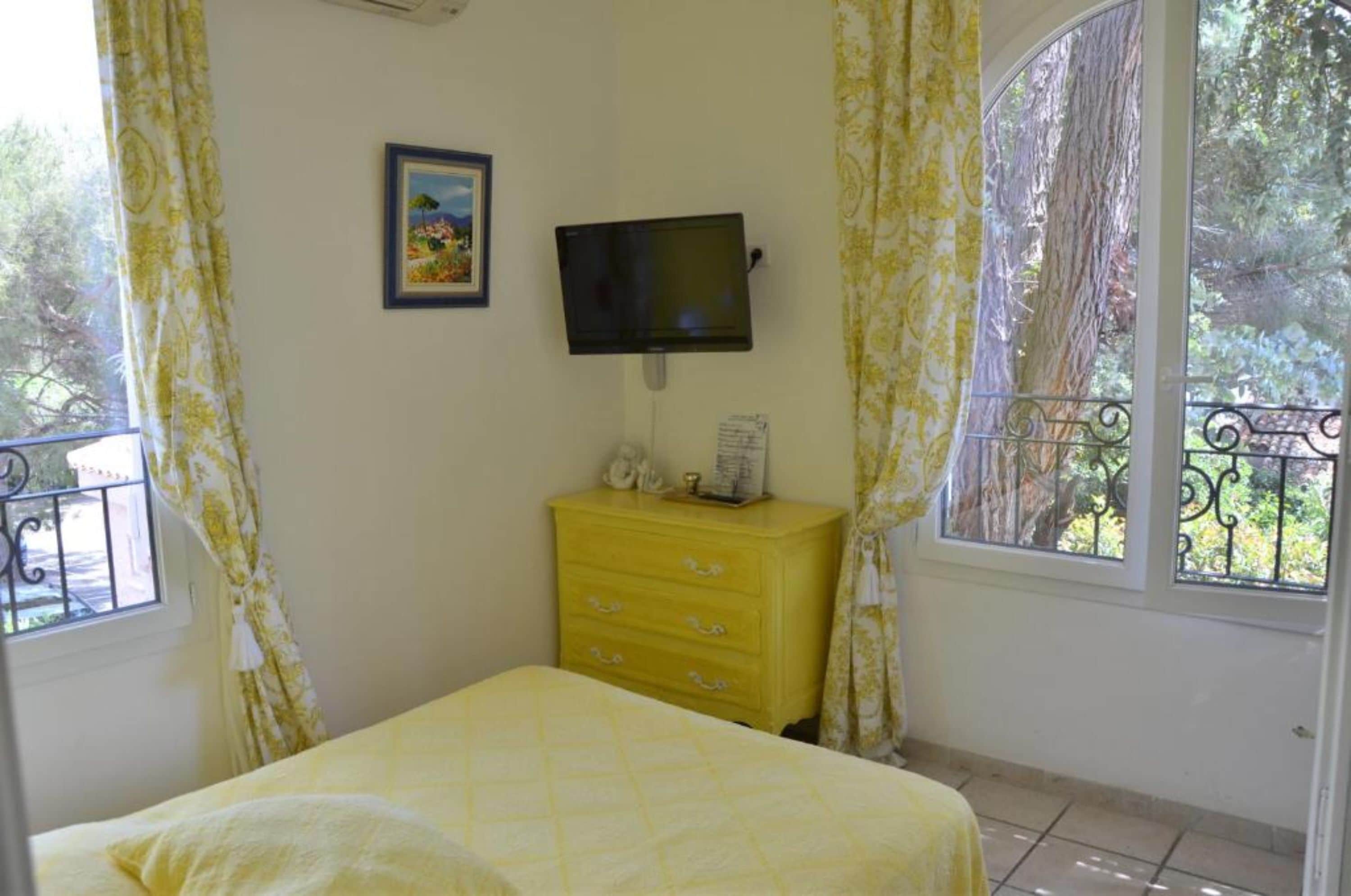 Una camera da letto con un letto, una televisione a muro, una cassettiera gialla e una finestra con tende.